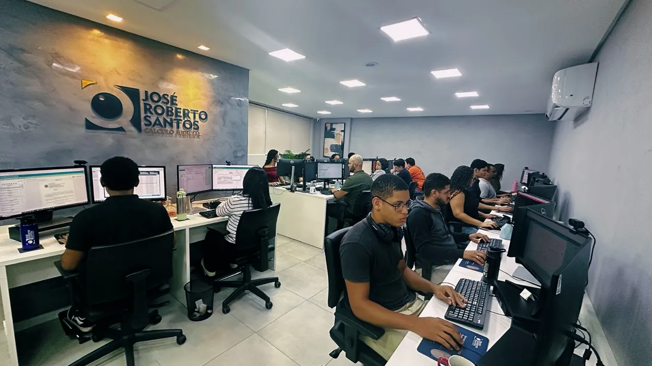 Estações de trabalho enfileiradas diante da parede com a marca José Roberto Santos em relevo.