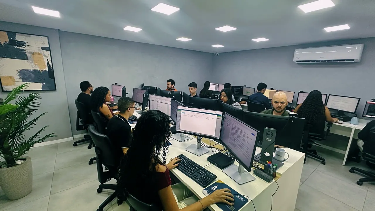 Equipe trabalhando em duas fileiras de estações, com quadro e planta no canto da sala.