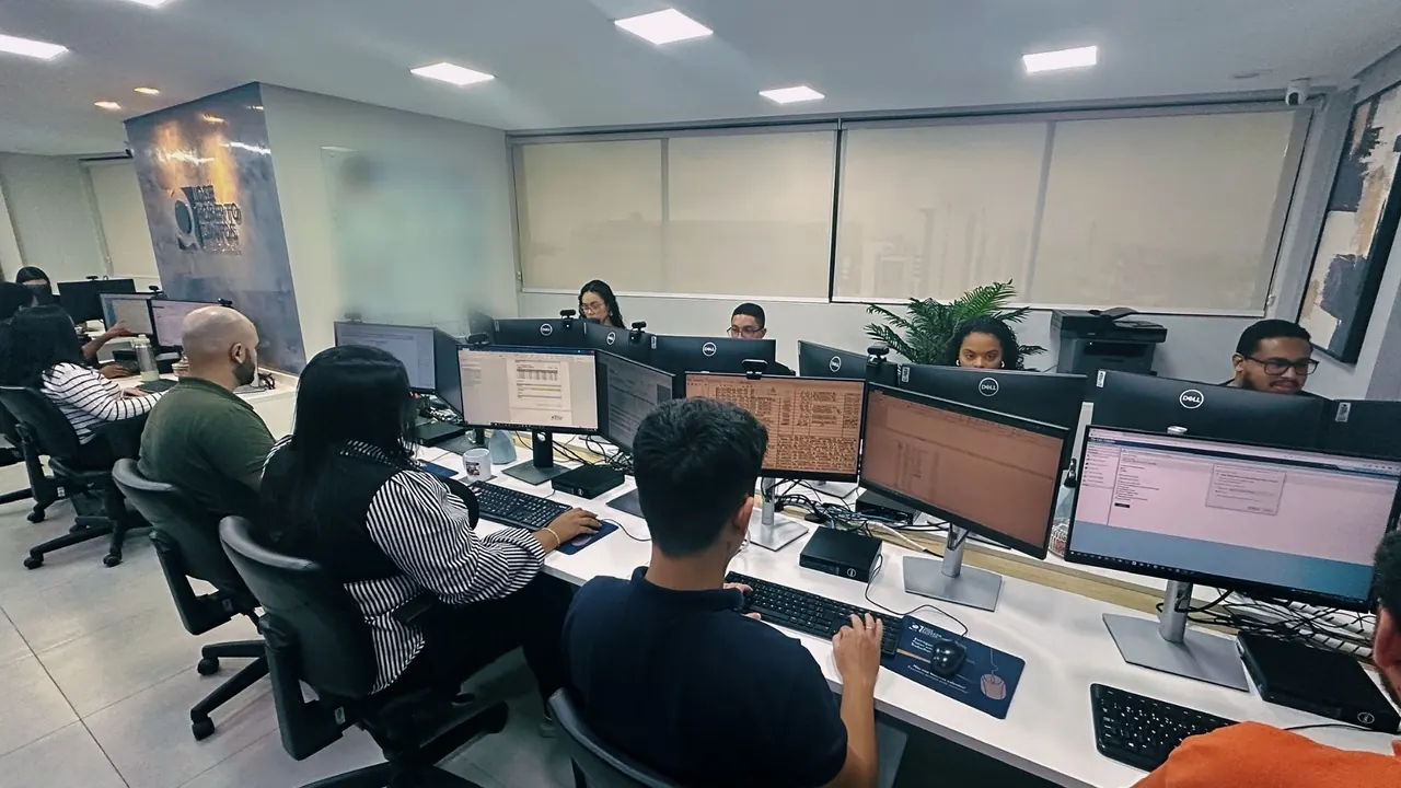 Equipe nas estações de frente para as janelas, com o quadro da rota de produção ao fundo.