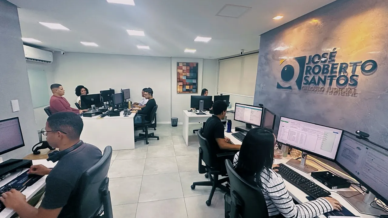 Contraplano da sala de produção, com a marca do escritório em relevo na parede à direita e as estações em duas fileiras.